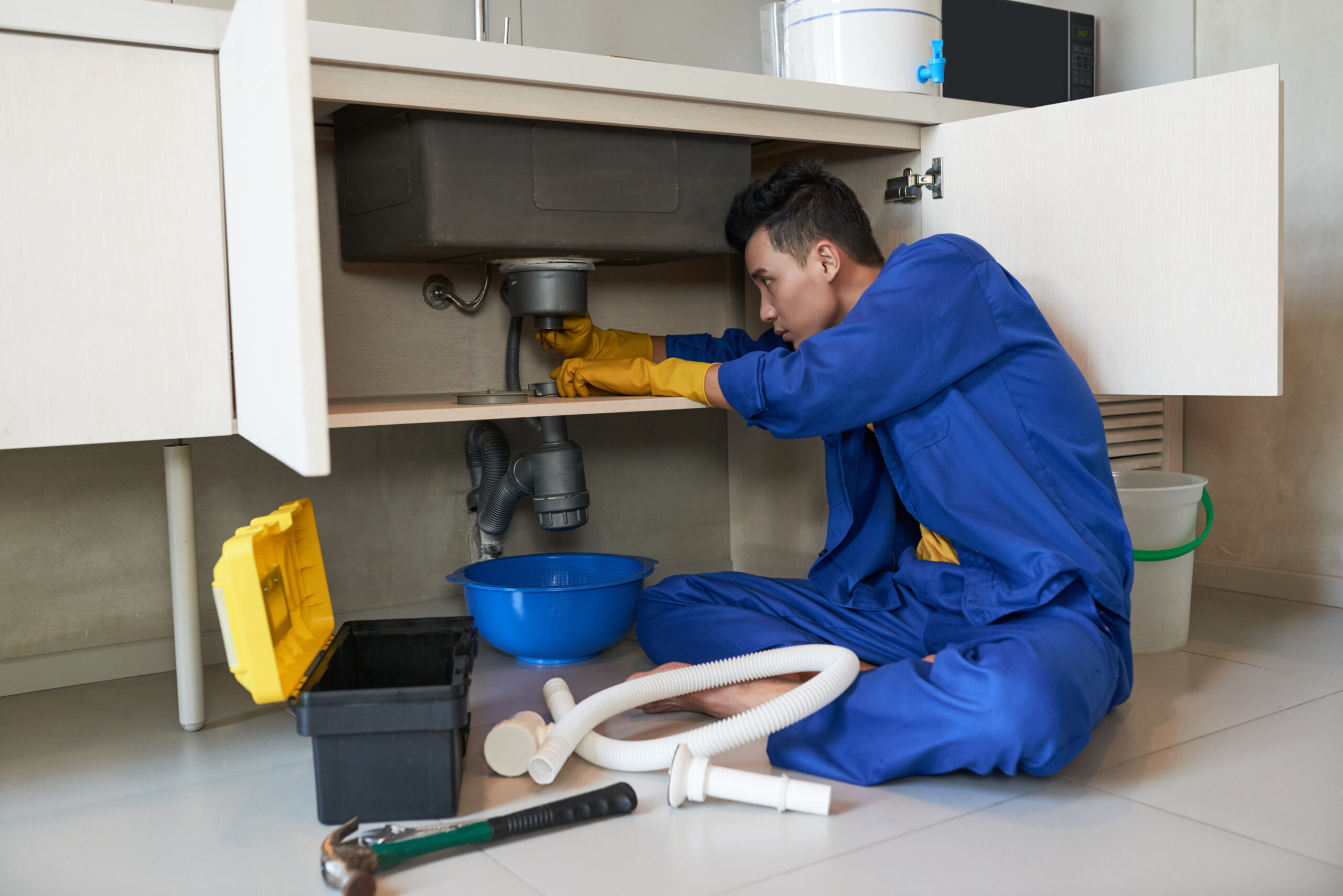Checking drain Young Vietnamese plumber checking drain in kitchen